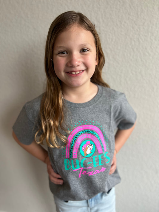 A child wearing a grey shirt with a pink and blue neon rainbow that reads Buc-ee's Texas