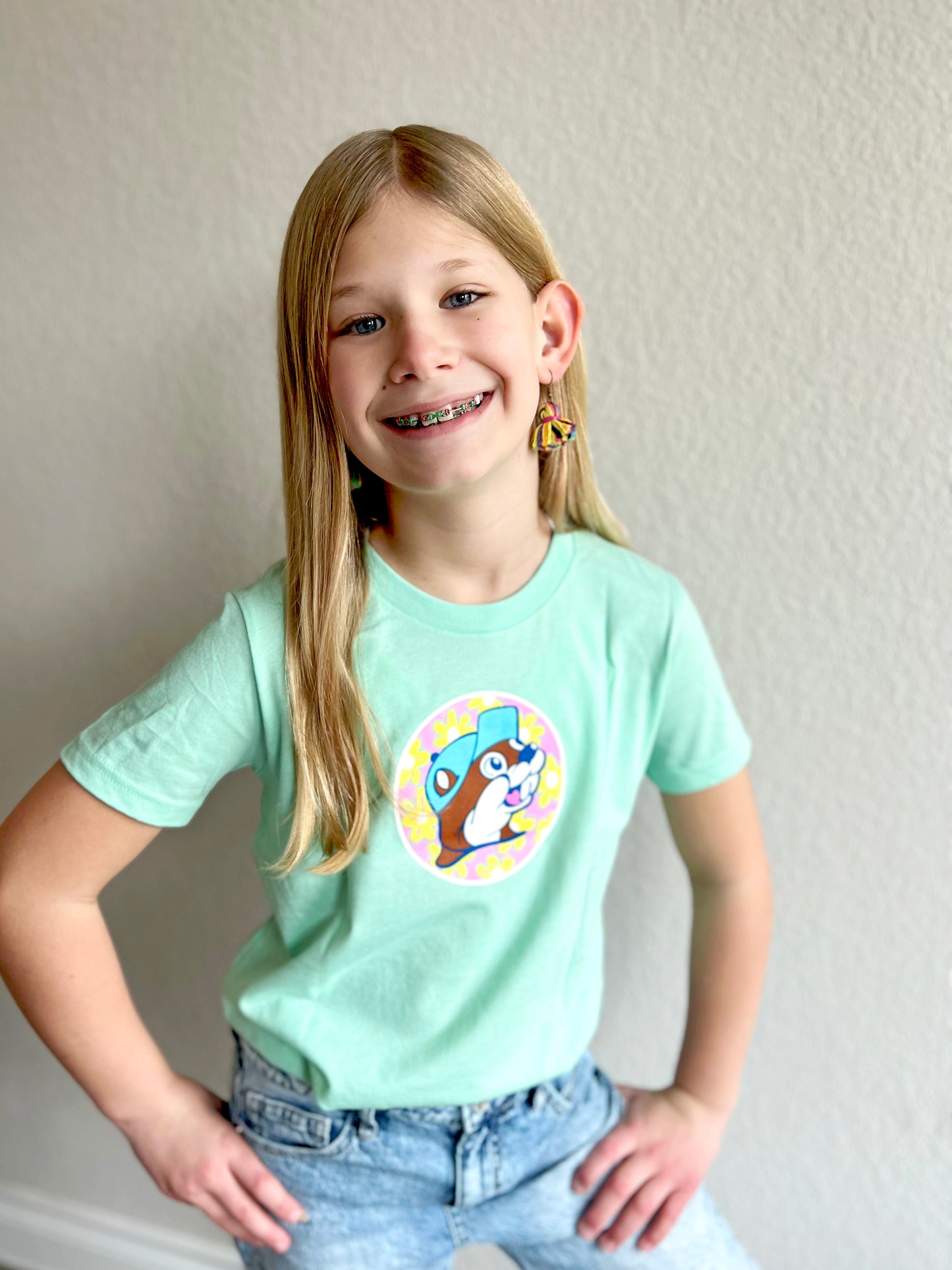 A girl wearing a mint shirt with a pink circle and yellow flowers with buc-ee's beaver inside