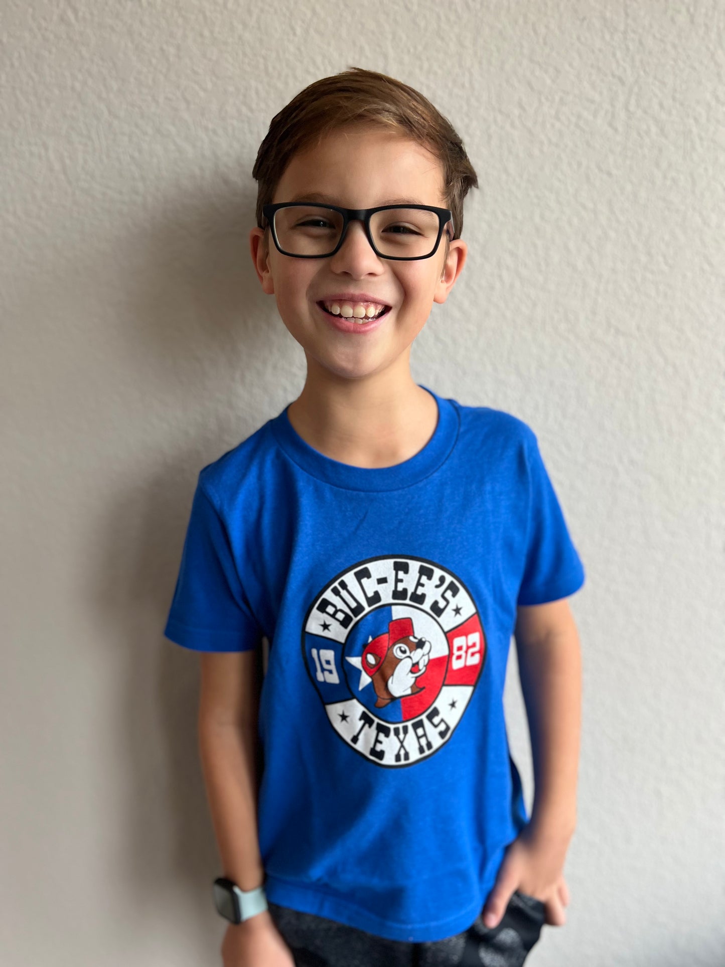 A boy wearing a blue Buc-ee's shirt. There is a white circle with black letters that read Buc-ee's Texas 1982